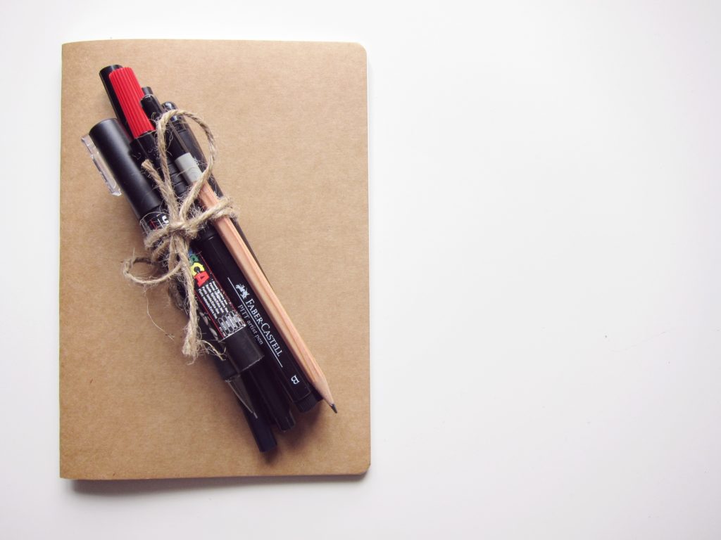 pens and pencil tied with string on brown notebook