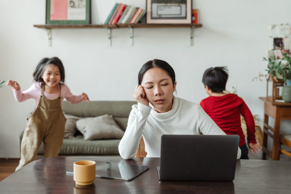 photo of mum at computer with kids racing around for post Setting Yourself Up For Writing Success